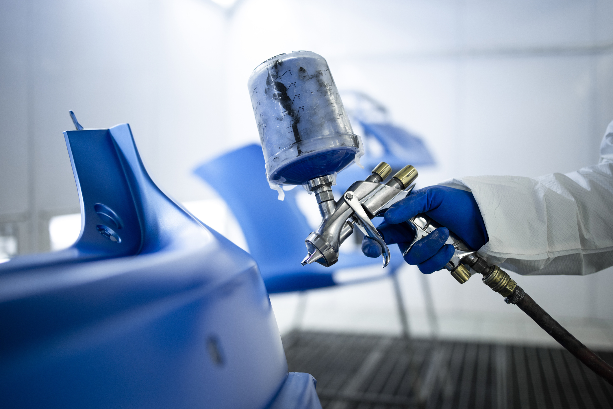 Technician applying paint to a body panel with a spray gun in the paint booth